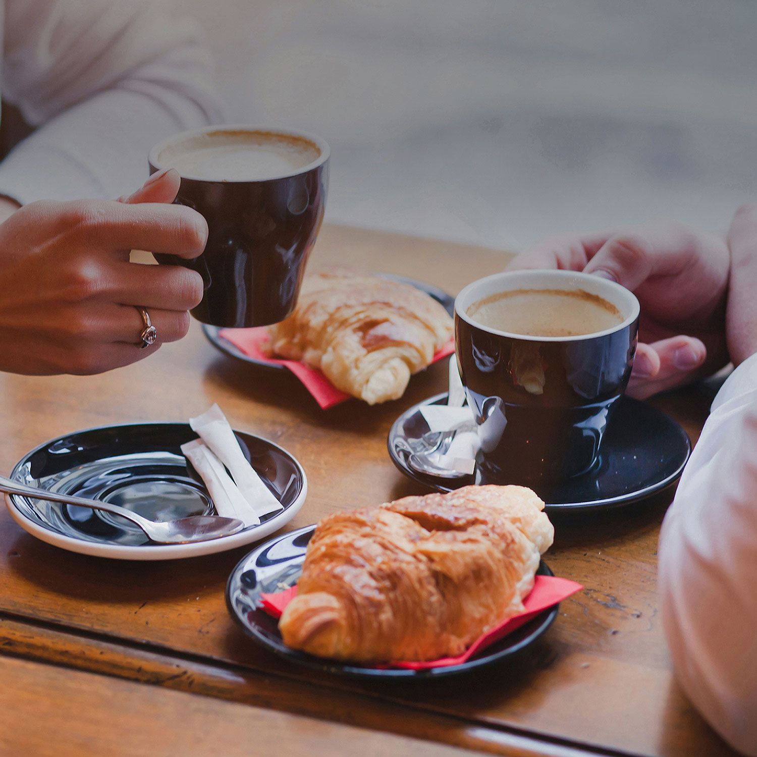 A breakfast table of croissants with two hands holding a cup of coffee